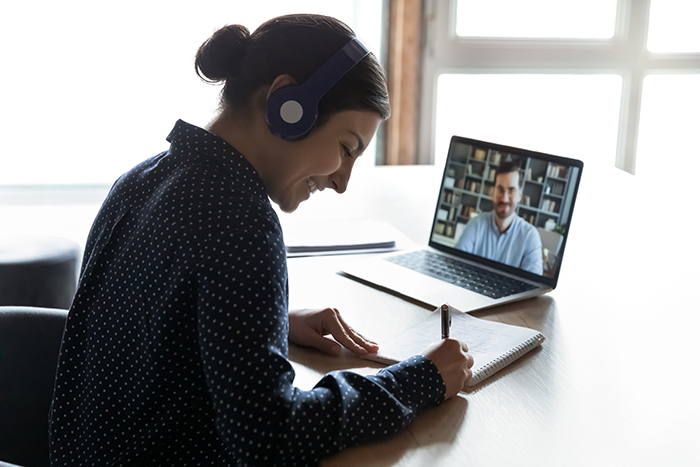 person watching webinar and taking notes, wearing headphones and smiling